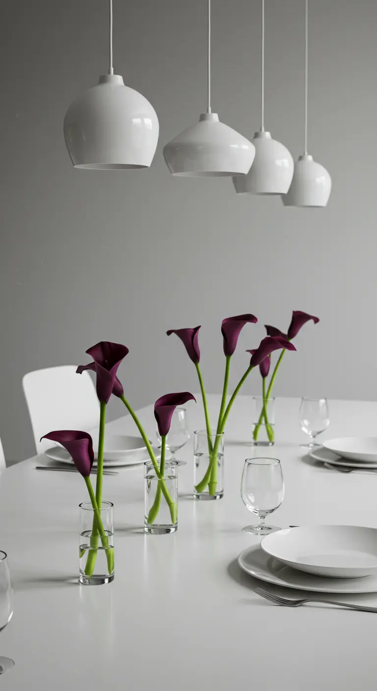 Single stems of dark purple calla lilies in individual glass vases on a white table.