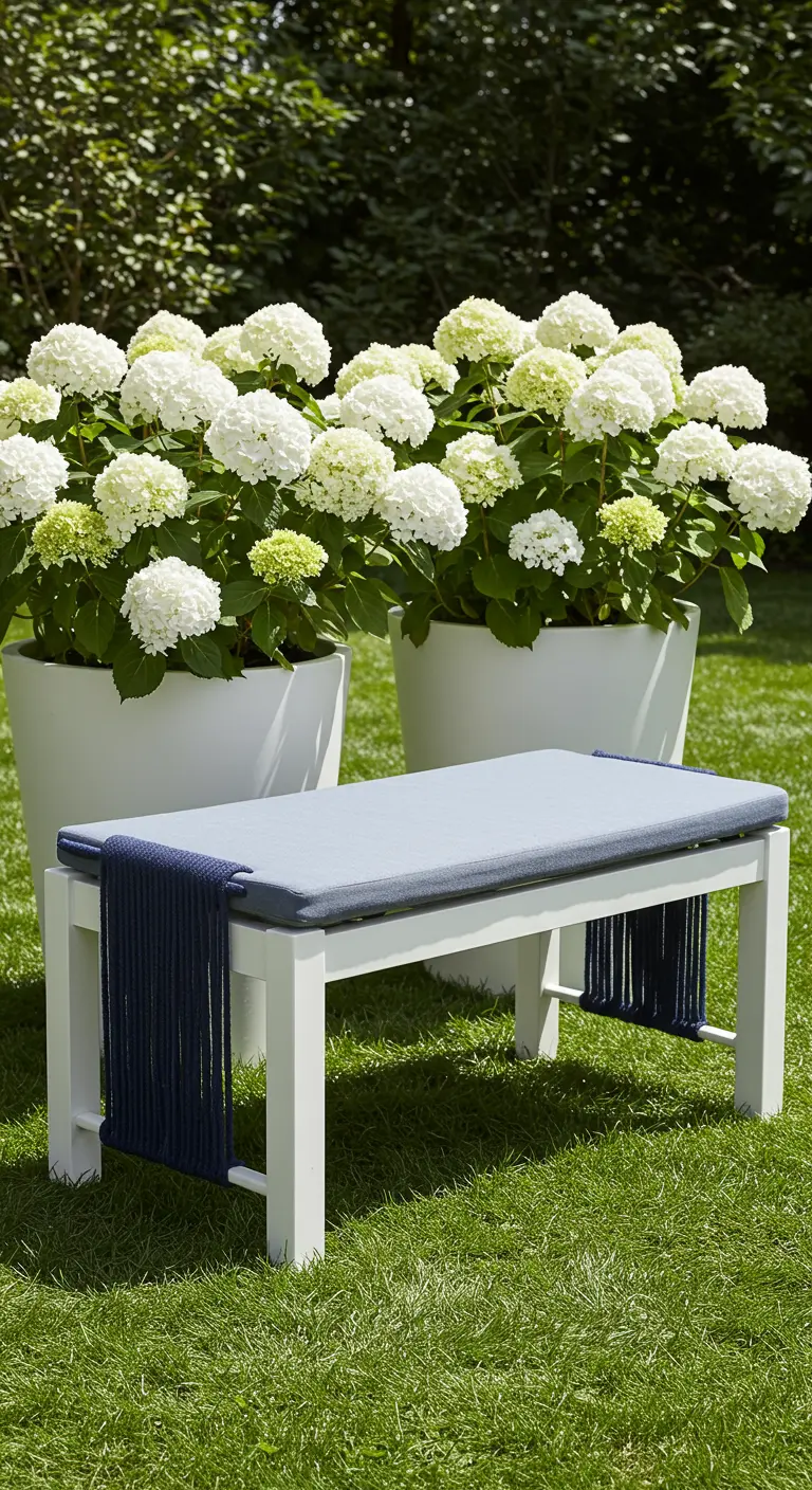 A crisp white bench with a dark navy woven rope seat in front of large white hydrangeas.