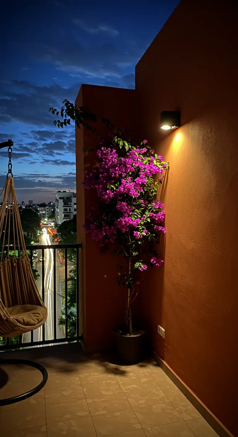 A high-rise balcony at night, with a spotlight illuminating a potted bougainvillea.