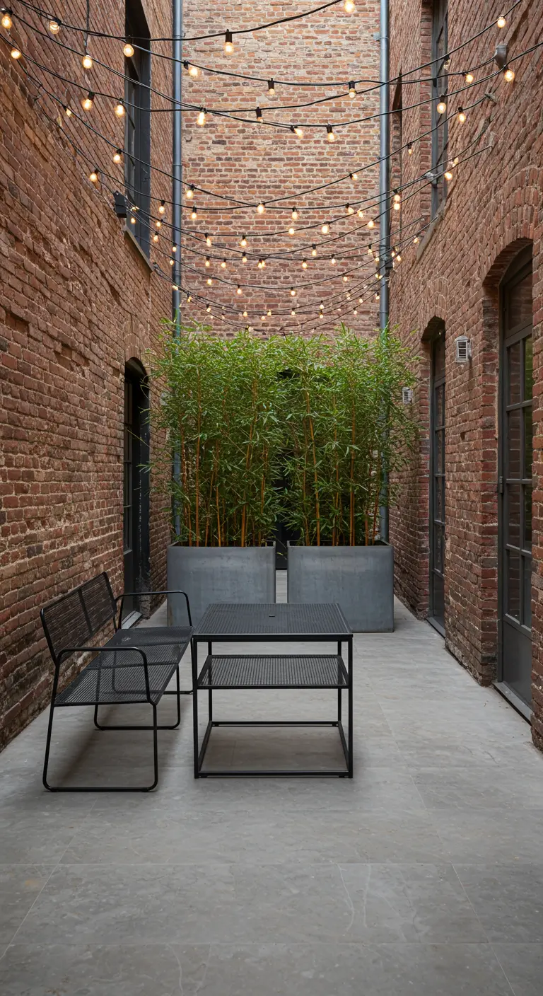 A narrow brick courtyard with tall bamboo planters and a black metal bench and table.