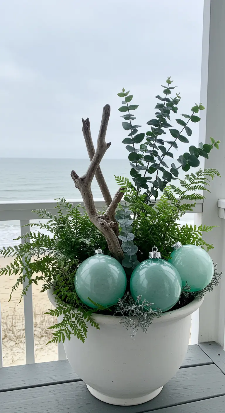A white planter on a coastal balcony with ferns, driftwood, and green baubles.