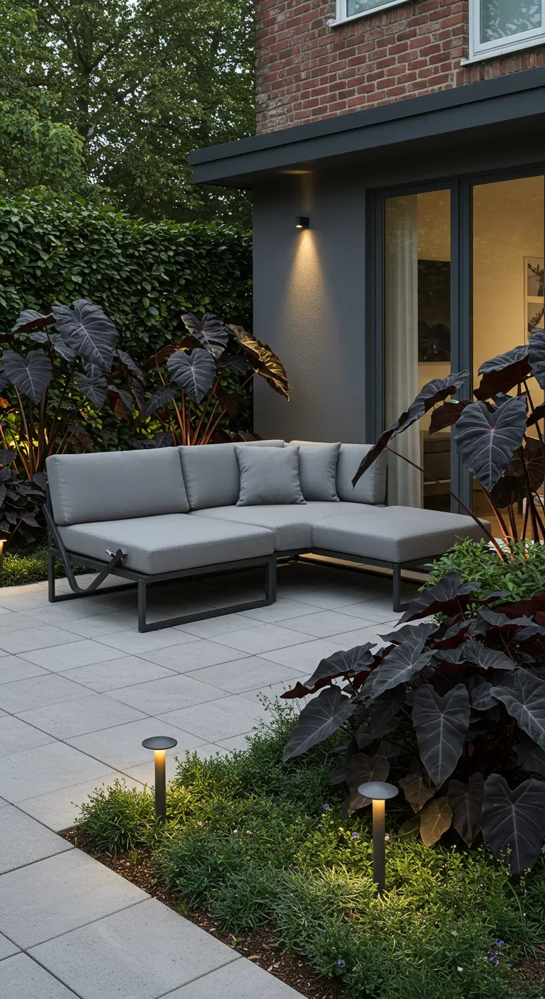 A modern patio with a grey sectional and dramatic, dark-leafed Elephant Ear plants.
