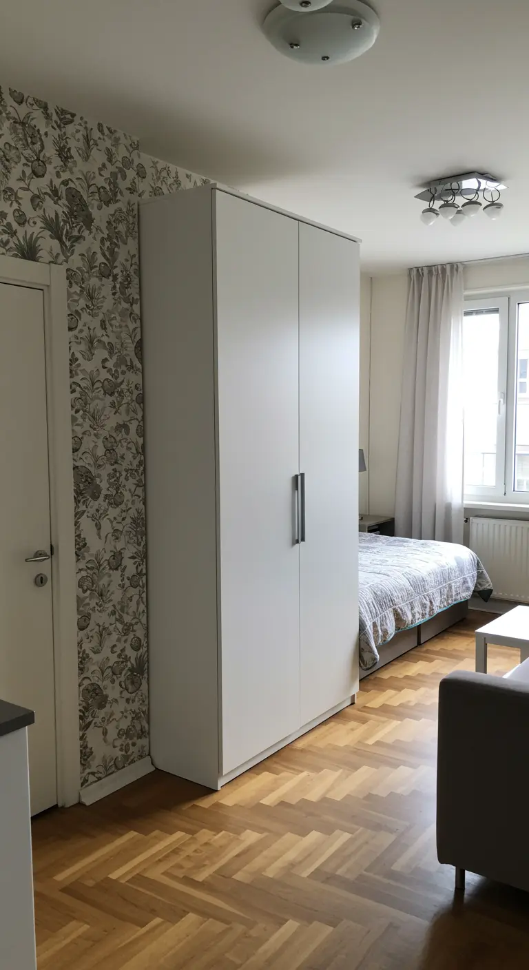 A tall white wardrobe stands between the living area and bed, acting as a room divider.