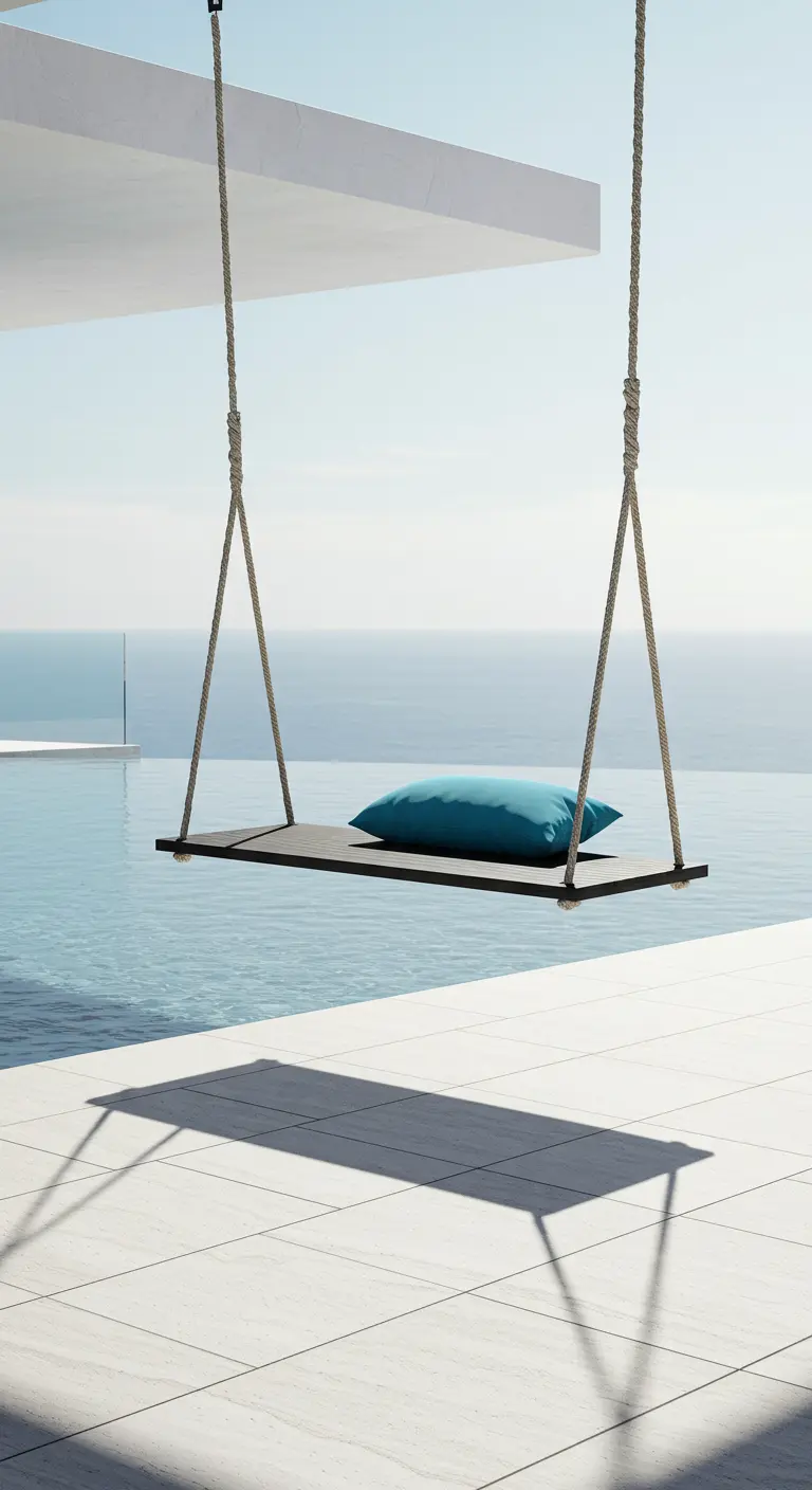 A simple plank swing with a blue pillow hanging over a modern patio with an ocean view.