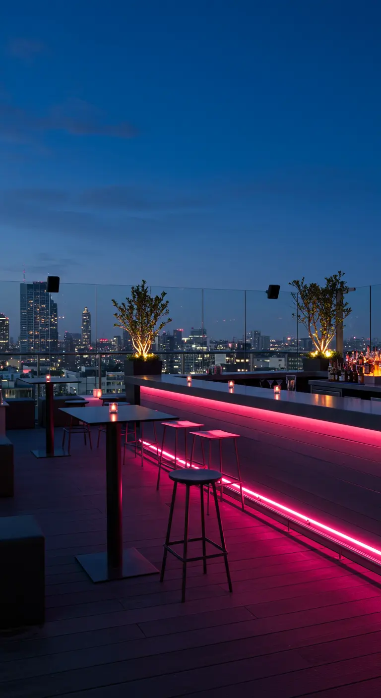 A modern rooftop bar at night with pink neon light strips under the counter.